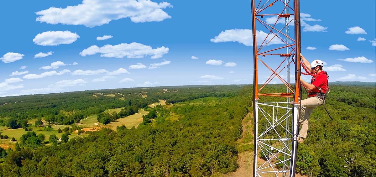 Aristotle High Speed Internet employee in helmet and safety gear climbs a tower on a sunny day