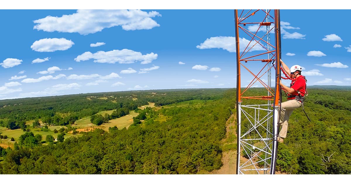 Aristotle High Speed Internet employee in helmet and safety gear climbs a tower on a sunny day