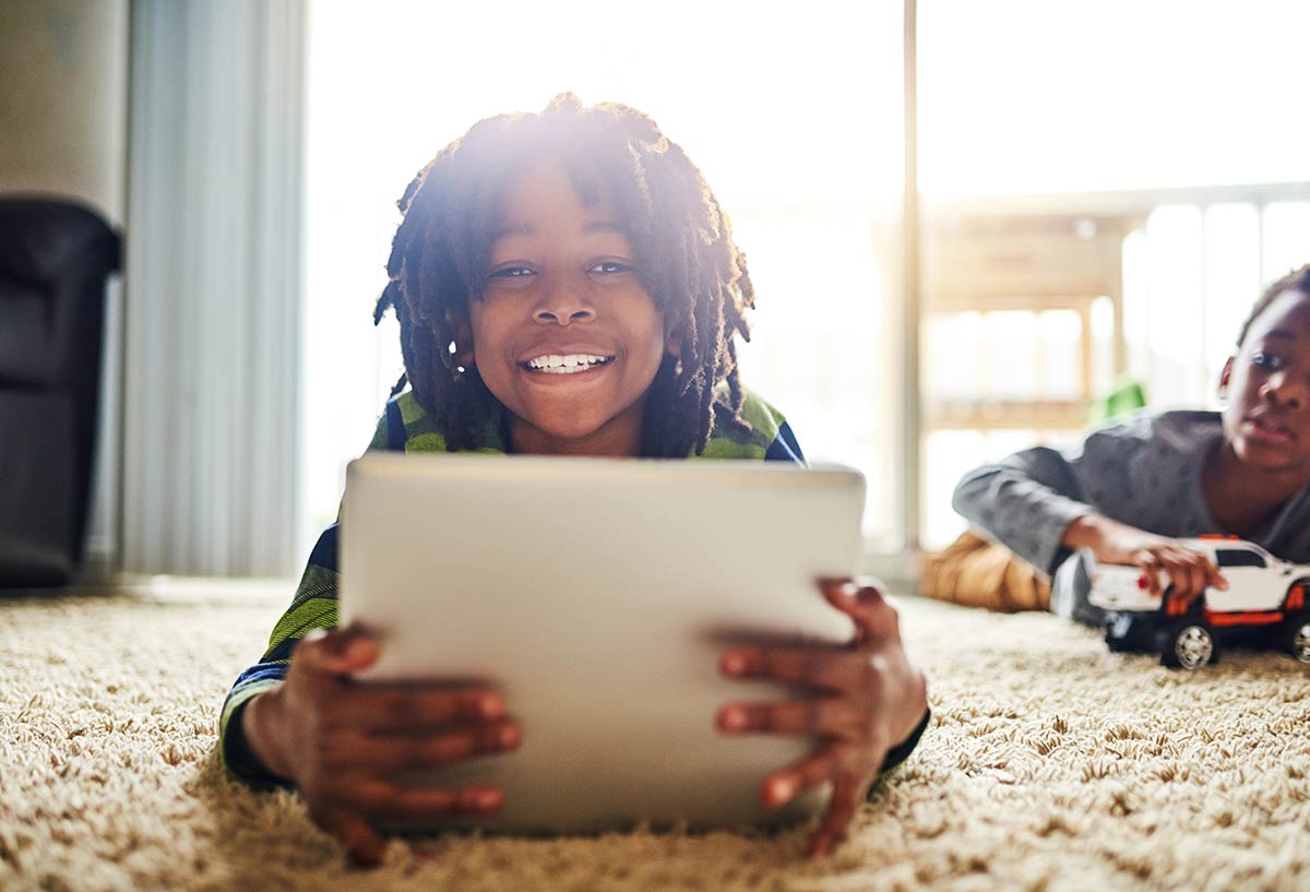 An African American boy enjoys streaming TV on a tablet device using ArisTV and Aristotle High Speed Internet
