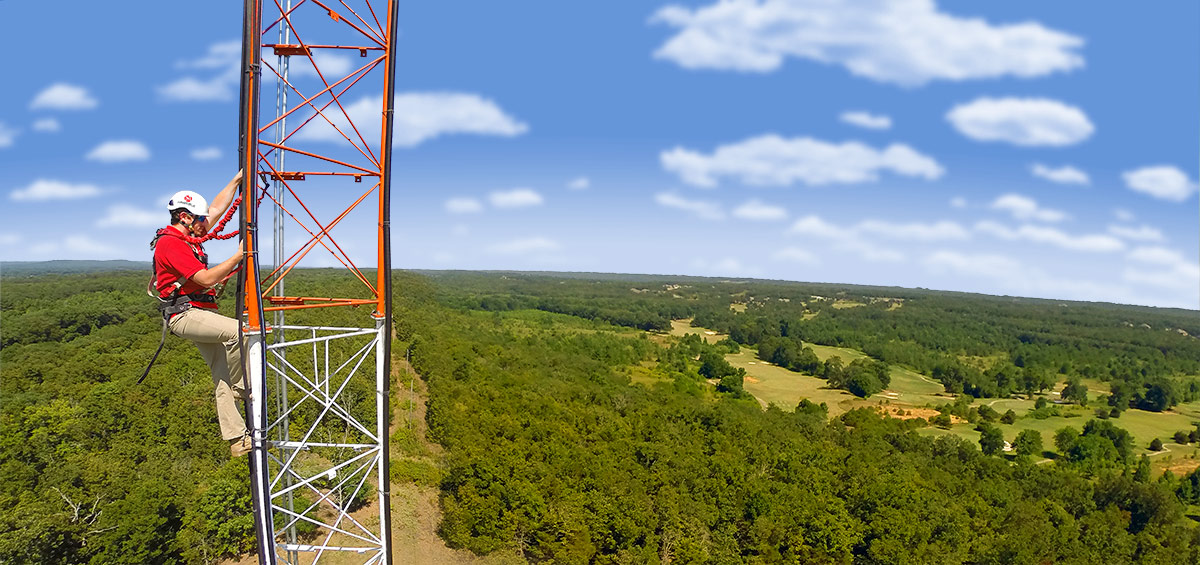 Aristotle High Speed Internet employee in helmet and safety gear climbs a tower on a sunny day